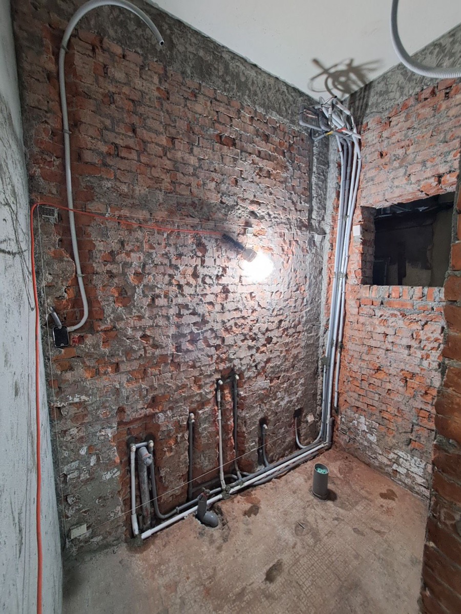 跨場域水電施工現場:老屋打除粉刷層後可見裸露磚牆,地坪沿牆腳重新埋設給排水配管,壁面與天花板可見新拉的電氣管路 rough-in 階段。