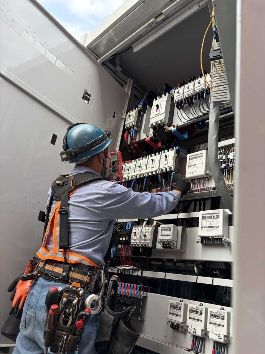 水電雄爸現場施作：身穿橙色安全背心、戴安全帽、配掛工具腰帶，於商業大樓電表暗箱前進行配電盤施作與檢修。